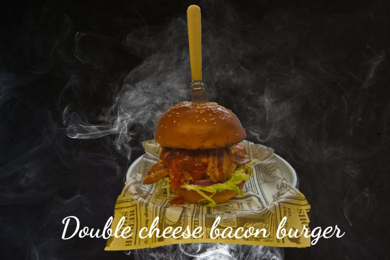 Double Cheese Bacon burger szeletelt bacon-nel és szósszal, füstös, sötét háttér előtt tálalva